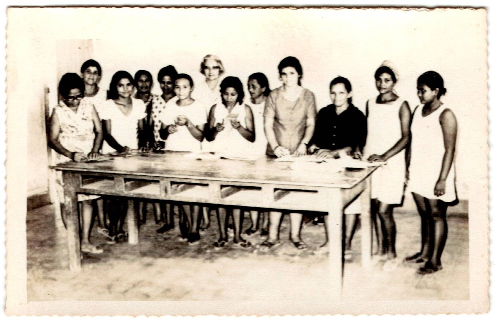 Moças reunidas em volta de uma mesa comprida de trabalho